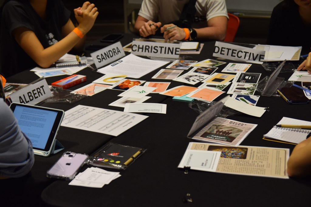 Documents, photos, and newspaper clippings on a table, with name cards in front of players