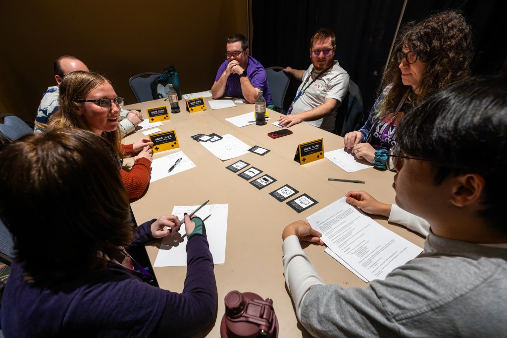 A group of players sitting around a table talking and reading documents